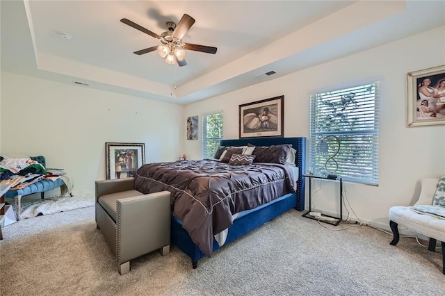 carpeted bedroom featuring a tray ceiling and ceiling fan