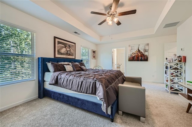 carpeted bedroom featuring a tray ceiling, multiple windows, ceiling fan, and connected bathroom