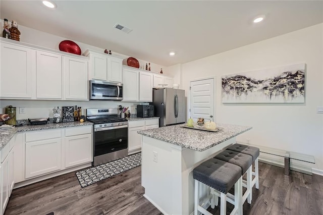 kitchen with light stone countertops, dark wood-type flooring, white cabinets, a kitchen island, and appliances with stainless steel finishes