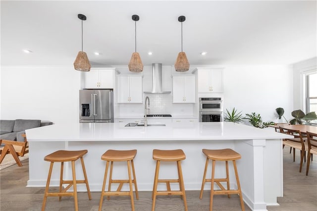 kitchen featuring a sink, backsplash, appliances with stainless steel finishes, wall chimney range hood, and a large island with sink