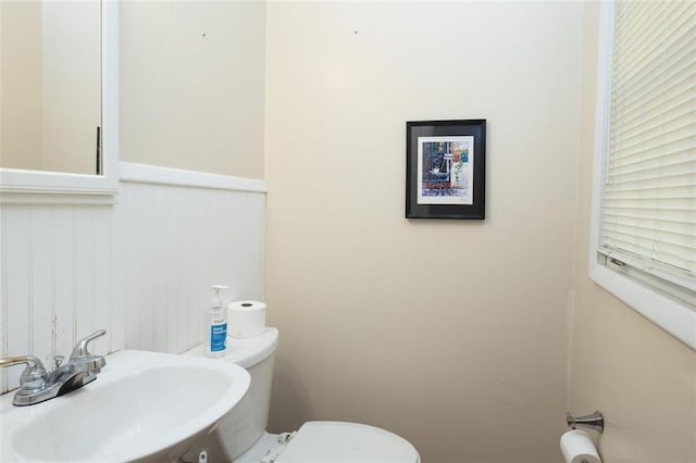 half bath with toilet, a wainscoted wall, and a sink