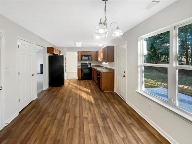 kitchen featuring brown cabinetry, pendant lighting, dark wood-style flooring, an inviting chandelier, and black appliances