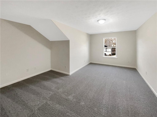 additional living space featuring baseboards, vaulted ceiling, and dark colored carpet