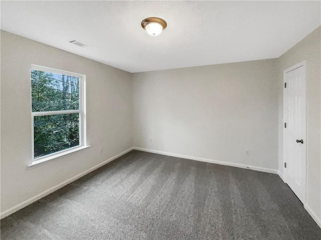 spare room featuring dark colored carpet, baseboards, and visible vents