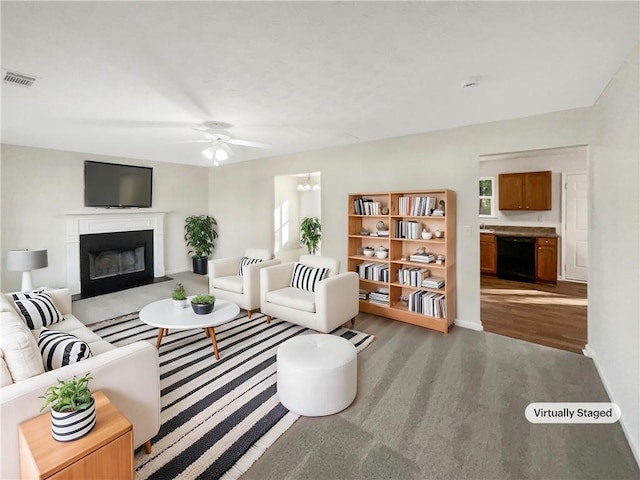 carpeted living room featuring a glass covered fireplace, a ceiling fan, baseboards, wood finished floors, and visible vents