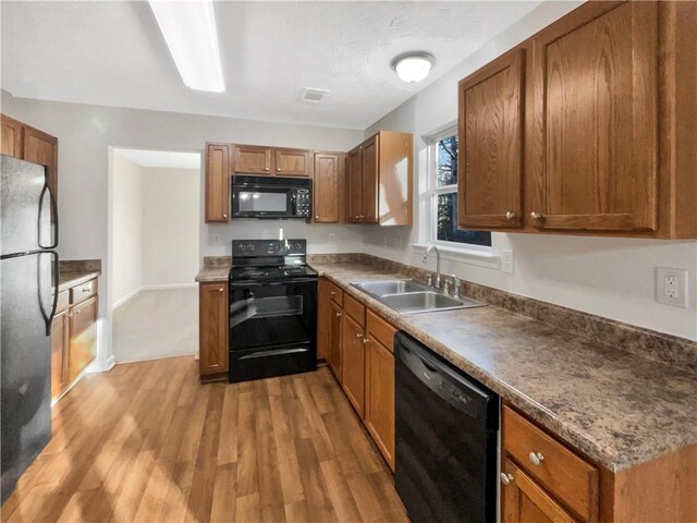 kitchen with brown cabinets, light wood-type flooring, a sink, baseboards, and black appliances