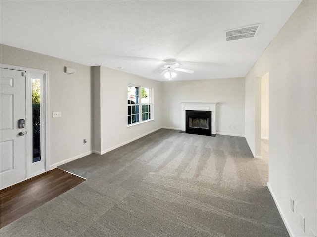 unfurnished living room with visible vents, carpet floors, a fireplace with flush hearth, baseboards, and a ceiling fan