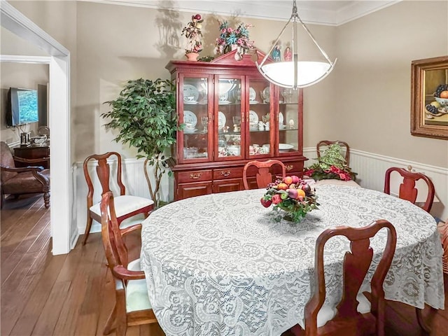 dining space with ornamental molding, wood-type flooring, and wainscoting