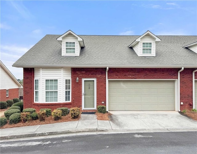 cape cod home with brick siding, an attached garage, driveway, and a shingled roof