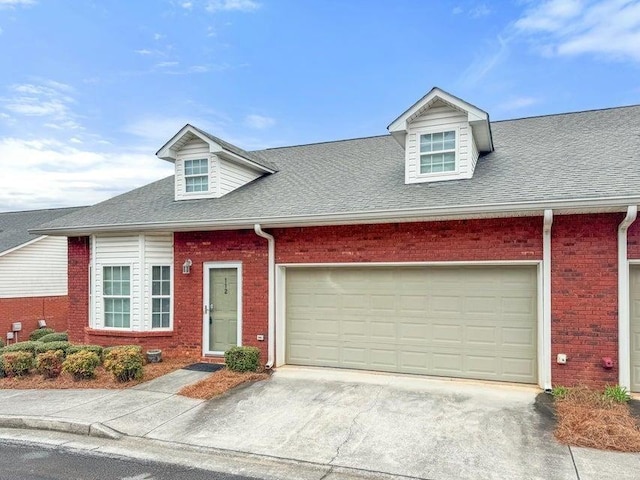 cape cod home with brick siding, an attached garage, concrete driveway, and roof with shingles