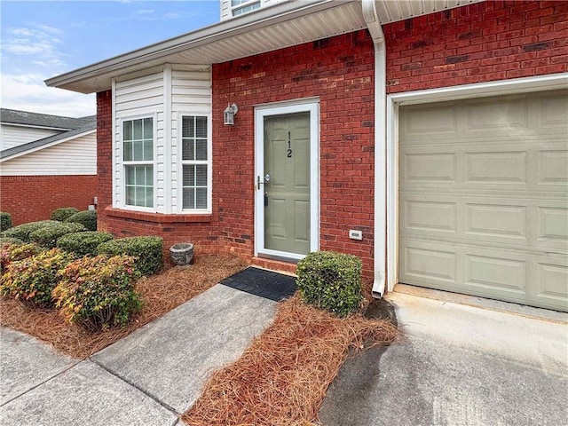 doorway to property featuring a garage and brick siding