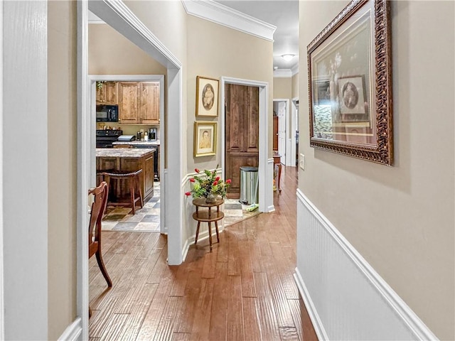 hall with light wood-type flooring, a wainscoted wall, and ornamental molding