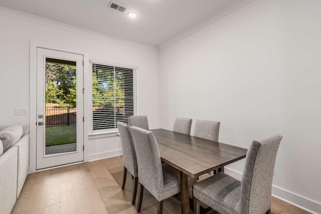 dining area with ornamental molding, light wood-type flooring, visible vents, and baseboards