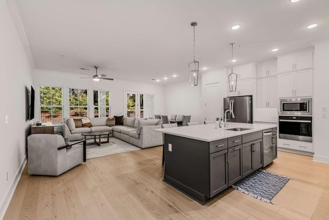 kitchen featuring stainless steel appliances, light countertops, light wood-style flooring, white cabinets, and a sink