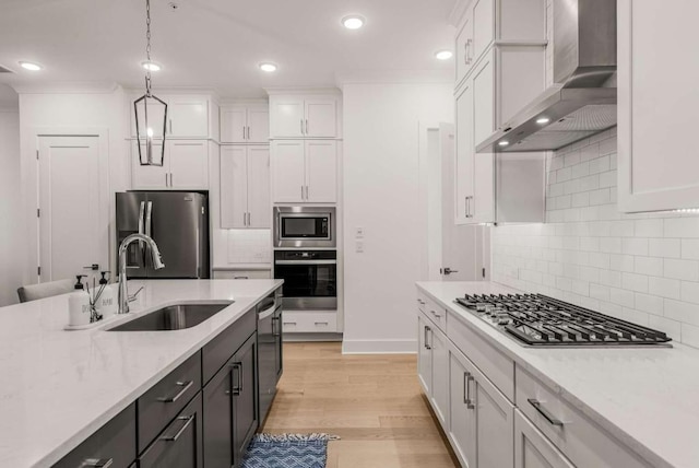 kitchen with white cabinets, wall chimney exhaust hood, stainless steel appliances, light countertops, and a sink