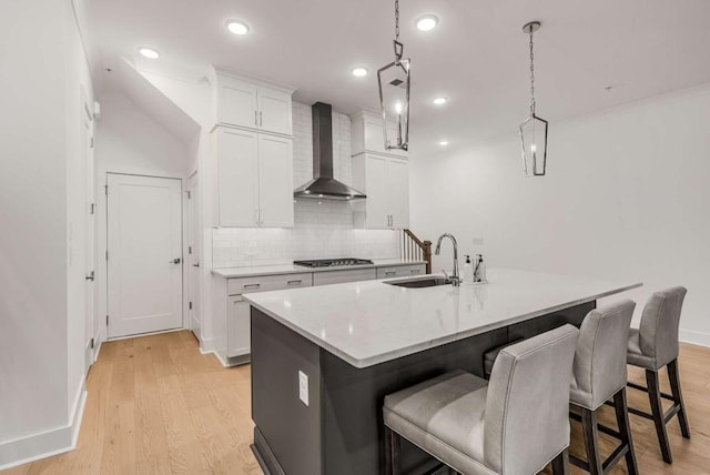 kitchen featuring wall chimney exhaust hood, a breakfast bar area, light wood-style floors, stainless steel gas cooktop, and a sink