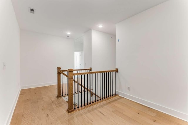 hall featuring visible vents, wood finished floors, an upstairs landing, and baseboards