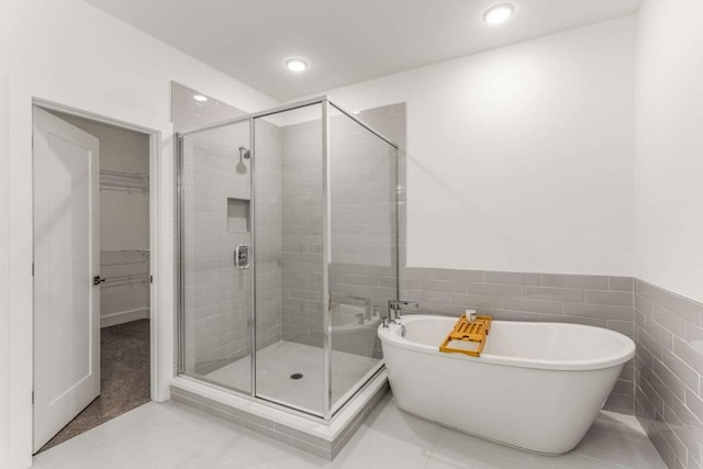 full bath featuring a stall shower, a soaking tub, tile patterned flooring, and a spacious closet