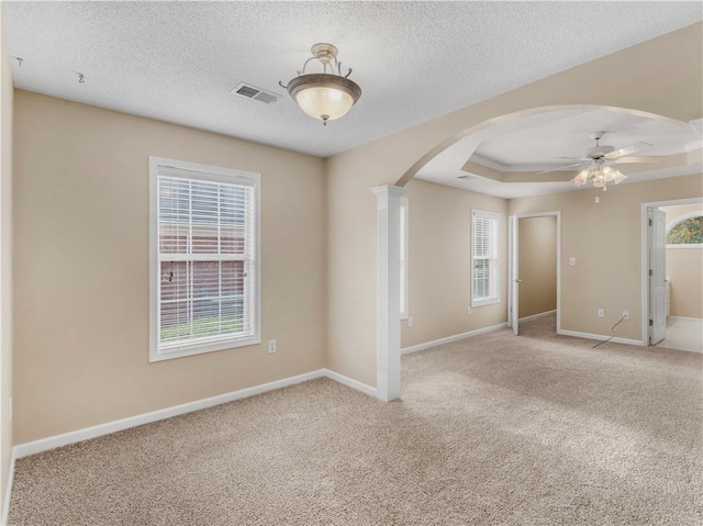 spare room with arched walkways, a textured ceiling, visible vents, baseboards, and carpet