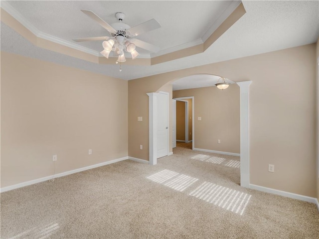 unfurnished room featuring ornamental molding, a tray ceiling, light carpet, and arched walkways