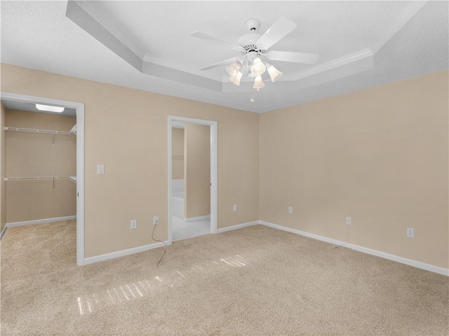 unfurnished bedroom with light carpet, baseboards, a tray ceiling, and a walk in closet