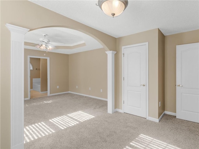 spare room featuring arched walkways, decorative columns, light carpet, ceiling fan, and baseboards