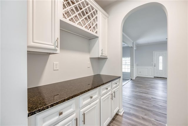 kitchen featuring dark stone counters, white cabinets, light wood-style flooring, and arched walkways