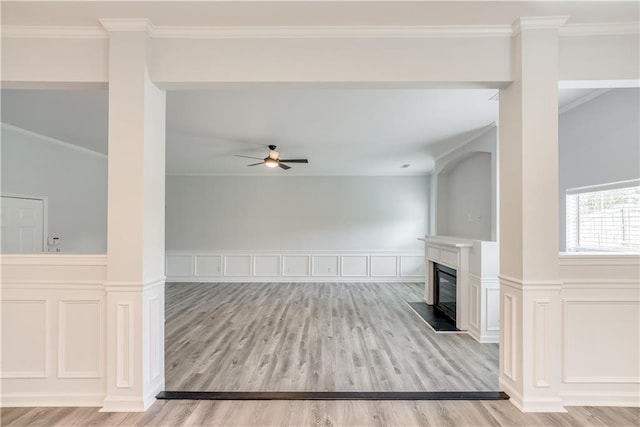 unfurnished living room featuring a glass covered fireplace, crown molding, light wood-style flooring, and ceiling fan