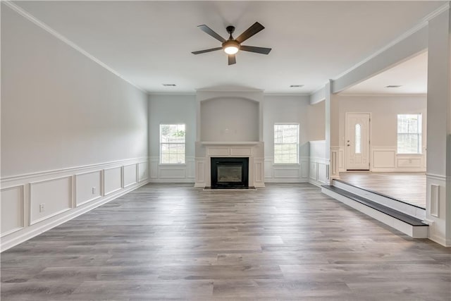 unfurnished living room featuring wood finished floors, a glass covered fireplace, a ceiling fan, and crown molding