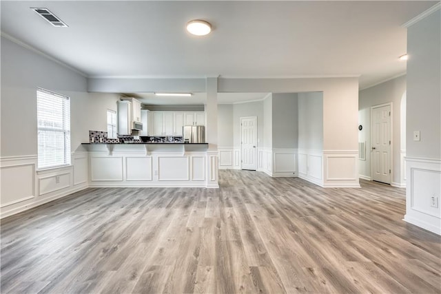 unfurnished living room featuring crown molding, light wood-style flooring, and visible vents