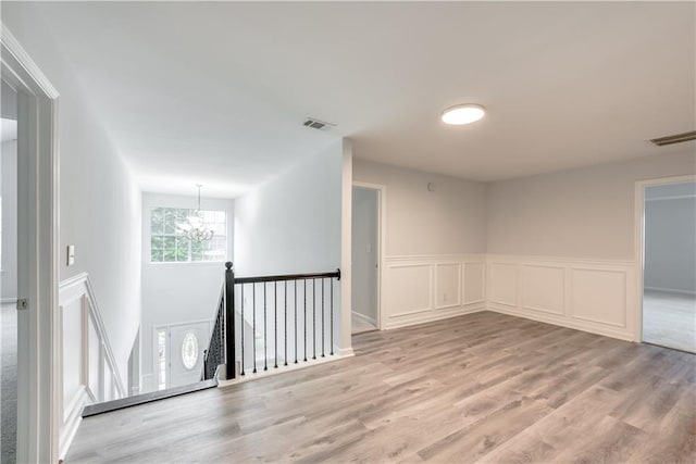 spare room featuring a notable chandelier, visible vents, light wood-type flooring, and a wainscoted wall