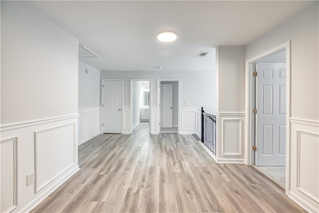 unfurnished room with visible vents, a decorative wall, attic access, and light wood finished floors