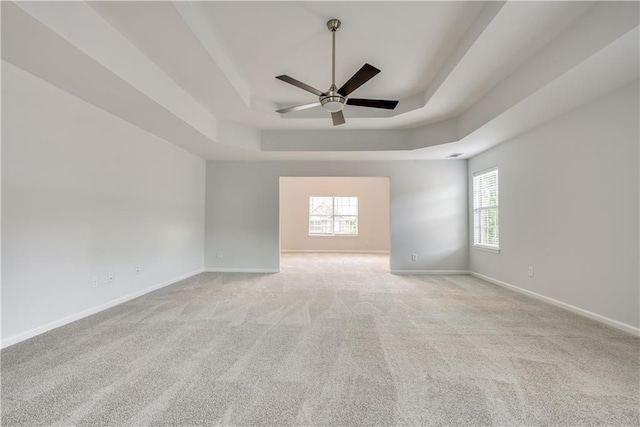 carpeted spare room featuring a tray ceiling, plenty of natural light, baseboards, and ceiling fan