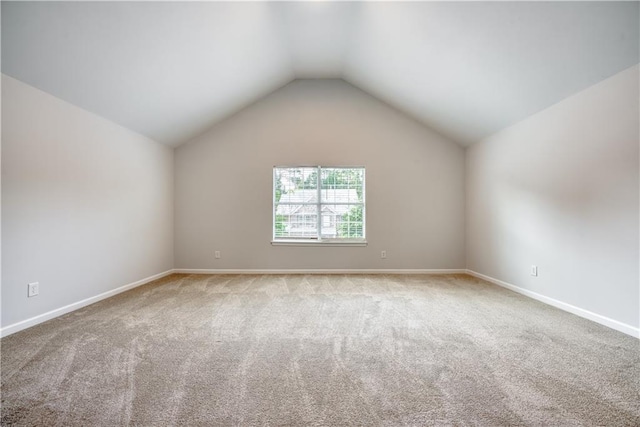 carpeted spare room with vaulted ceiling and baseboards