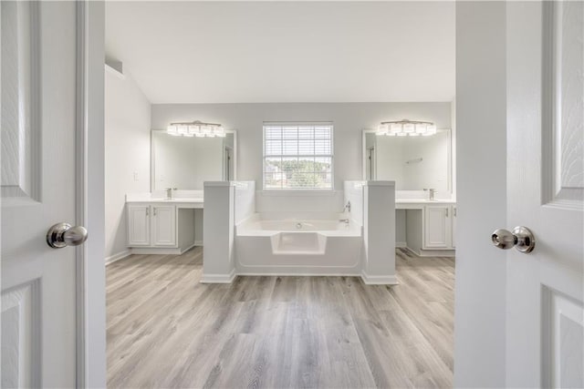 bathroom featuring two vanities, a sink, wood finished floors, baseboards, and a bath