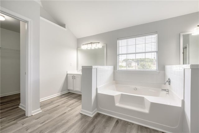 full bath with wood finished floors, baseboards, a bath, vanity, and vaulted ceiling