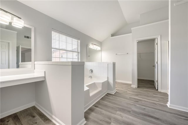 full bath with wood finished floors, visible vents, lofted ceiling, a spacious closet, and a garden tub