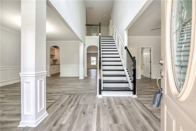 foyer entrance with arched walkways, light wood-style floors, a decorative wall, stairs, and ornate columns