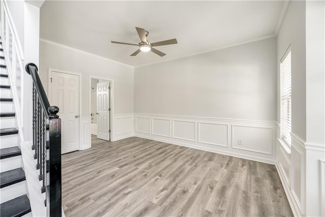 interior space with a wainscoted wall, ceiling fan, stairs, light wood-style floors, and crown molding