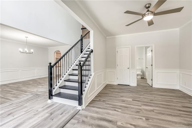 staircase featuring a decorative wall, wood finished floors, and ceiling fan with notable chandelier