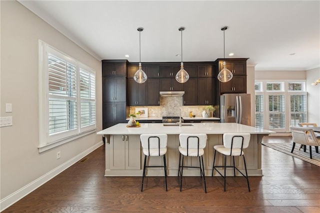 kitchen featuring a breakfast bar, hanging light fixtures, stainless steel refrigerator with ice dispenser, tasteful backsplash, and an island with sink