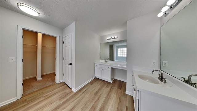 full bath with wood finished floors, baseboards, two vanities, a sink, and a textured ceiling