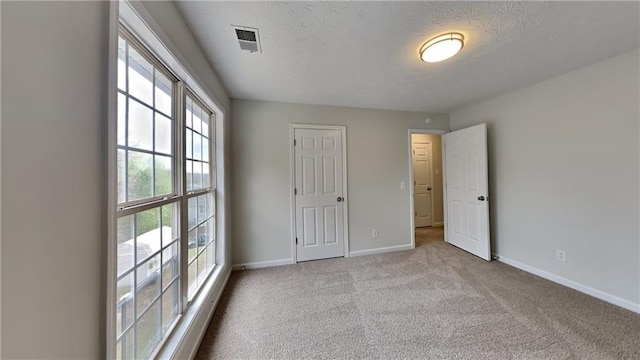 unfurnished bedroom with visible vents, carpet floors, a textured ceiling, and baseboards