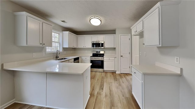 kitchen with visible vents, light countertops, appliances with stainless steel finishes, a peninsula, and a sink