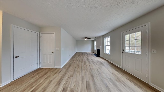 interior space with baseboards, a textured ceiling, light wood-style flooring, and a fireplace