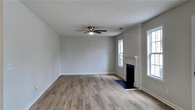 unfurnished living room with a textured ceiling, a healthy amount of sunlight, a ceiling fan, and a fireplace with raised hearth