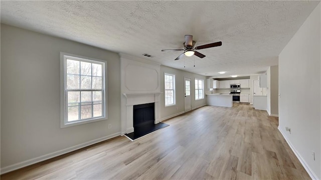 unfurnished living room featuring light wood-style flooring, a ceiling fan, visible vents, and a fireplace with raised hearth