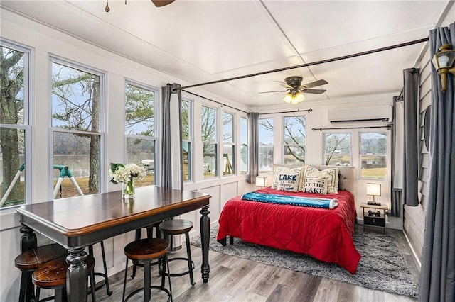 bedroom featuring multiple windows, wood finished floors, and an AC wall unit