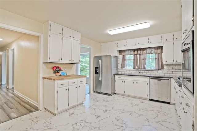 4025 Cheoah Dr, Douglasville, GA 30135 - kitchen featuring appliances with stainless steel finishes, a sink, decorative backsplash, white cabinets, and light marble finish flooring