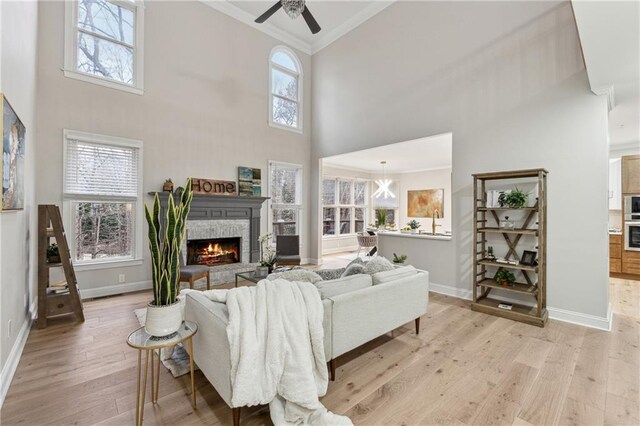 living room with light wood-style floors, a wealth of natural light, crown molding, and a stone fireplace